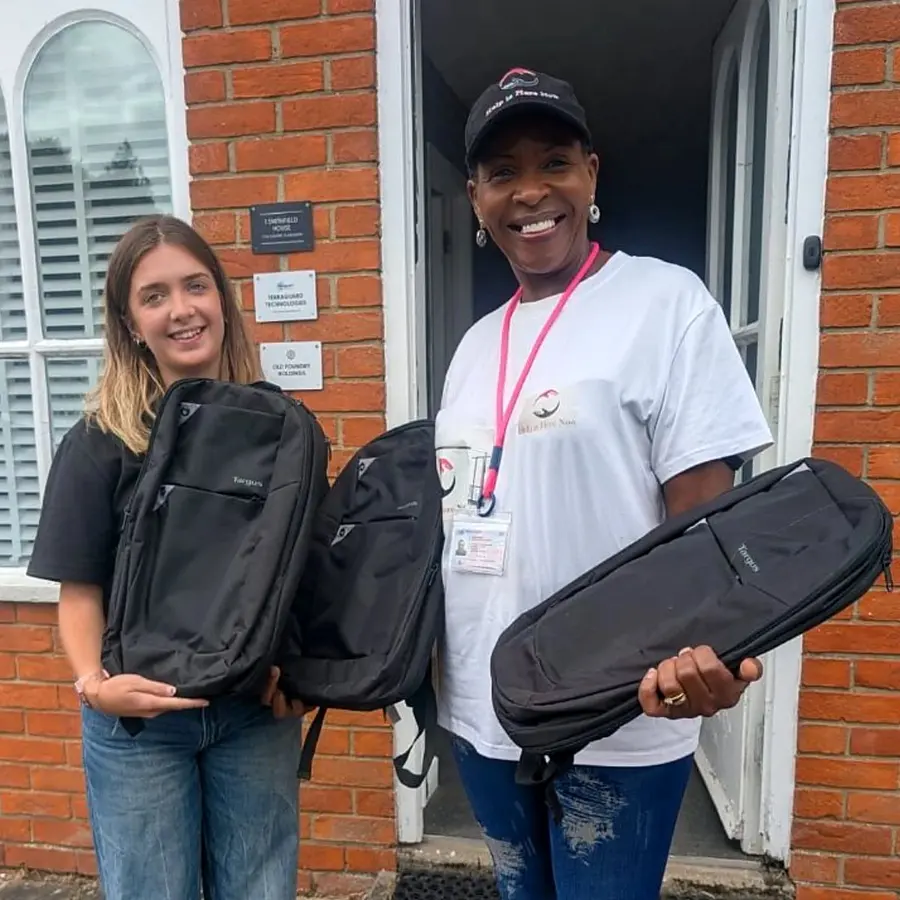 Two Terraguard staff outside the Aldbourne office, handing over donated laptop bags to a representative from A Good Thing