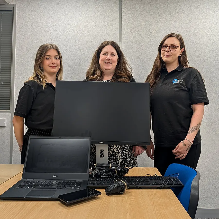 Three Terraguard staff behind a desk with a monitor, laptop, phone and keyboard, prepared for donation to Still Here Support Group