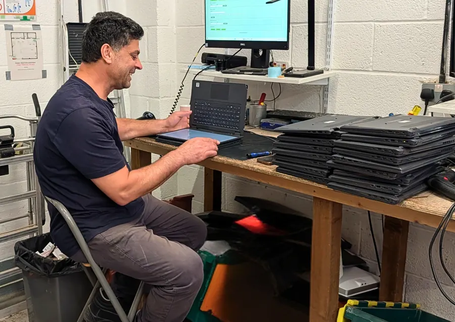 A technician testing a laptop at the refurbishment bench, with more laptops waiting beside them