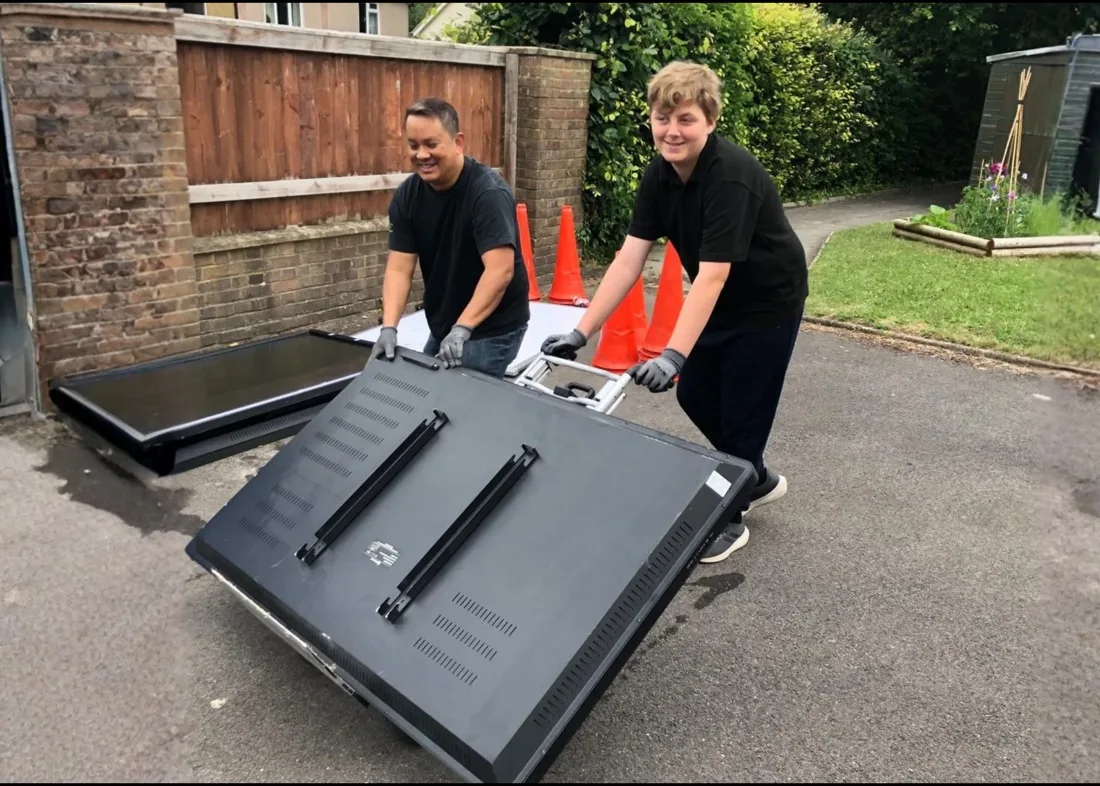 Two people wheeling large screens out for collection in Swindon